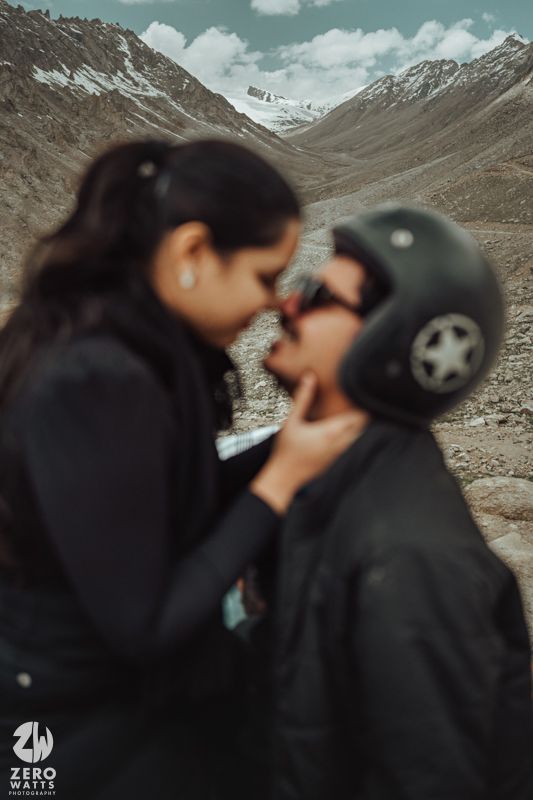 A couple shares an intimate moment against a backdrop of snow-capped mountains and dramatic mountain valley landscape.