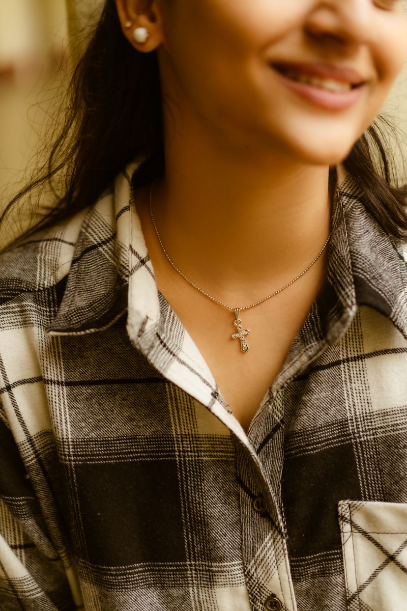 A close-up view of a delicate necklace pendant worn with a plaid flannel shirt.