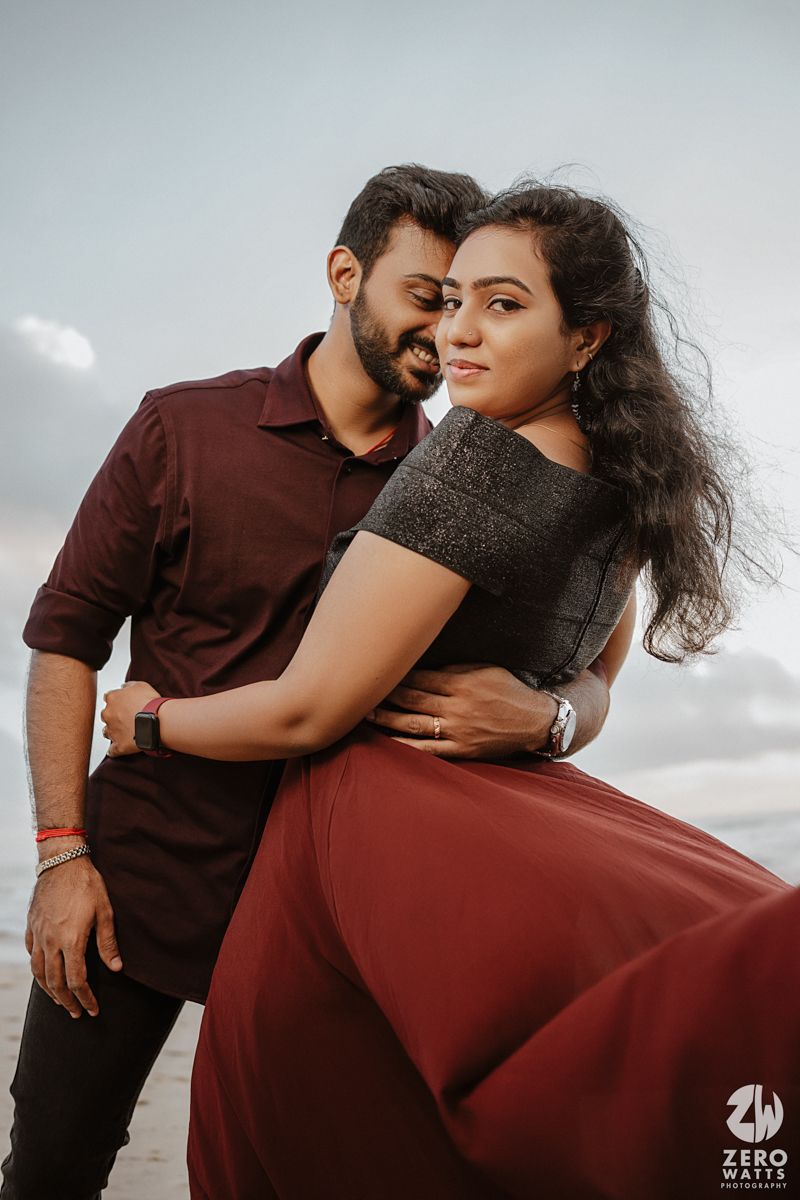 Romantic couple in matching burgundy outfits posing together against cloudy sky.