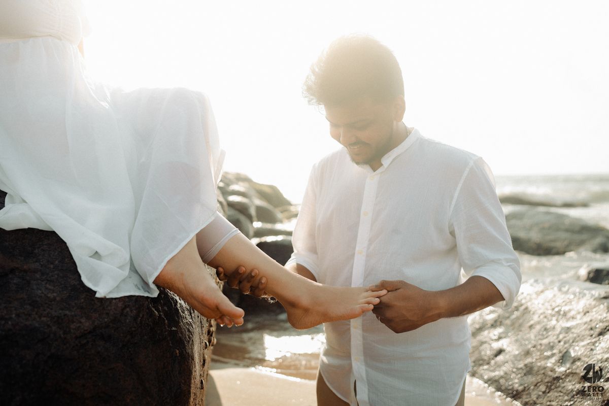 A couple shares an intimate moment on a rocky beach during golden hour.