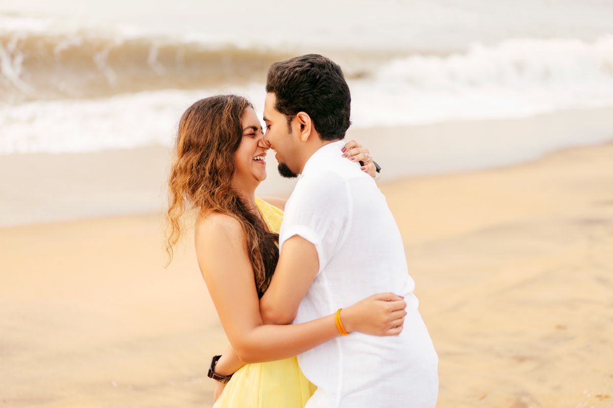Romantic couple embracing on a sandy beach at sunset in warm golden light.