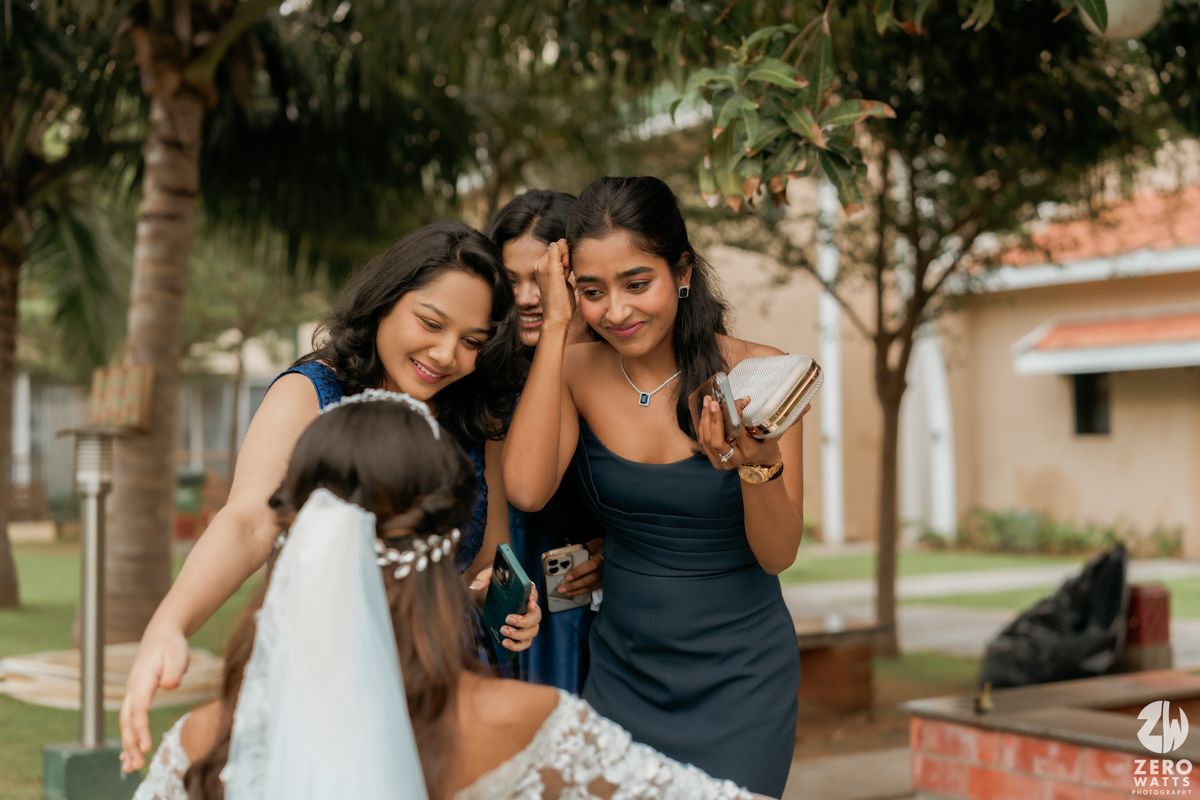 Three women blowing bubbles outdoors on a sunny day next to palm trees and buildings.