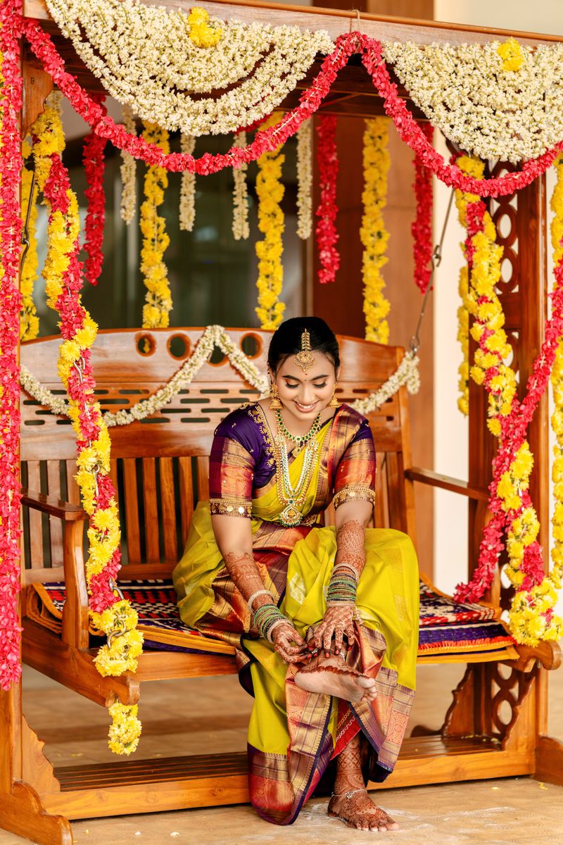 Traditional Indian bridal preparation scene with yellow and purple silk saree under floral decorations.