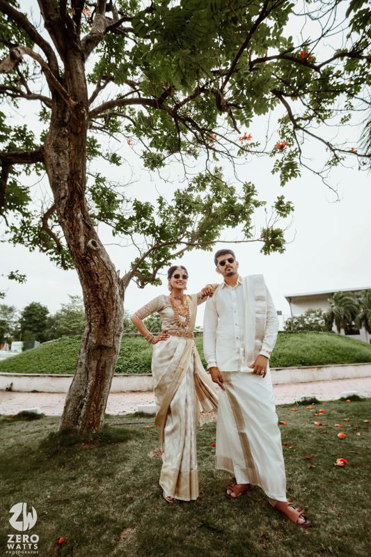 Traditional South Indian wedding photoshoot under trees with couple in elegant cream and white outfits.