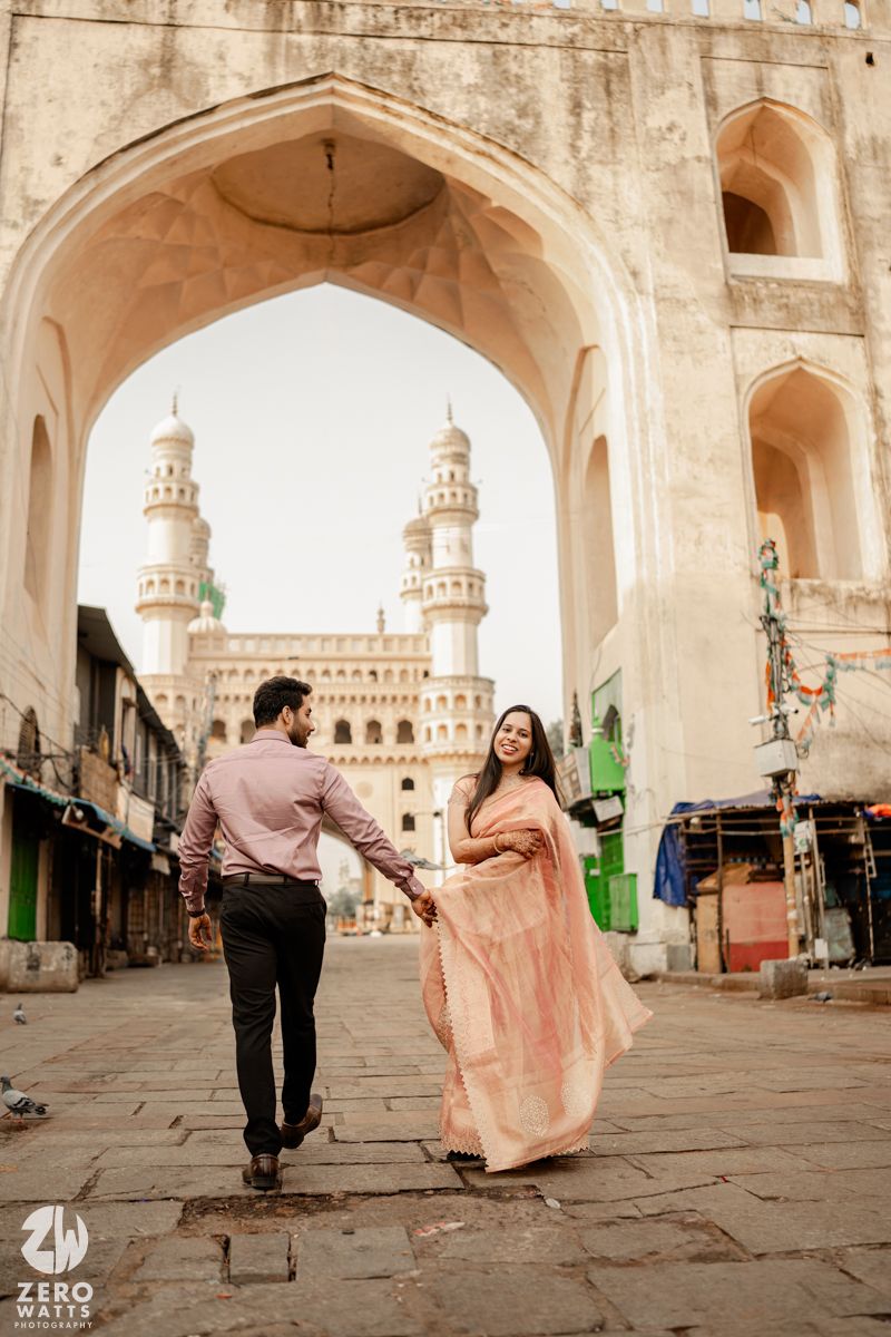 A romantic stroll through a historic archway with minarets and Charminar architecture in the background.