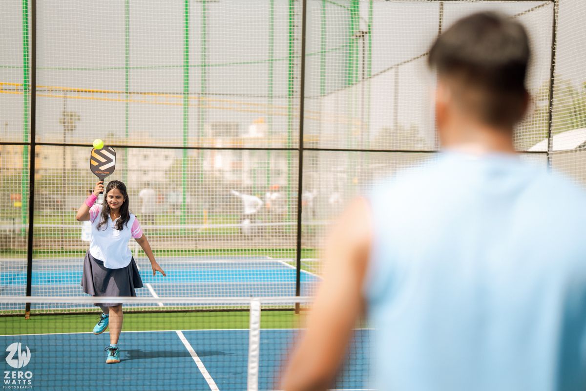 Couple playing tennis together on an outdoor court with a green surface and net.