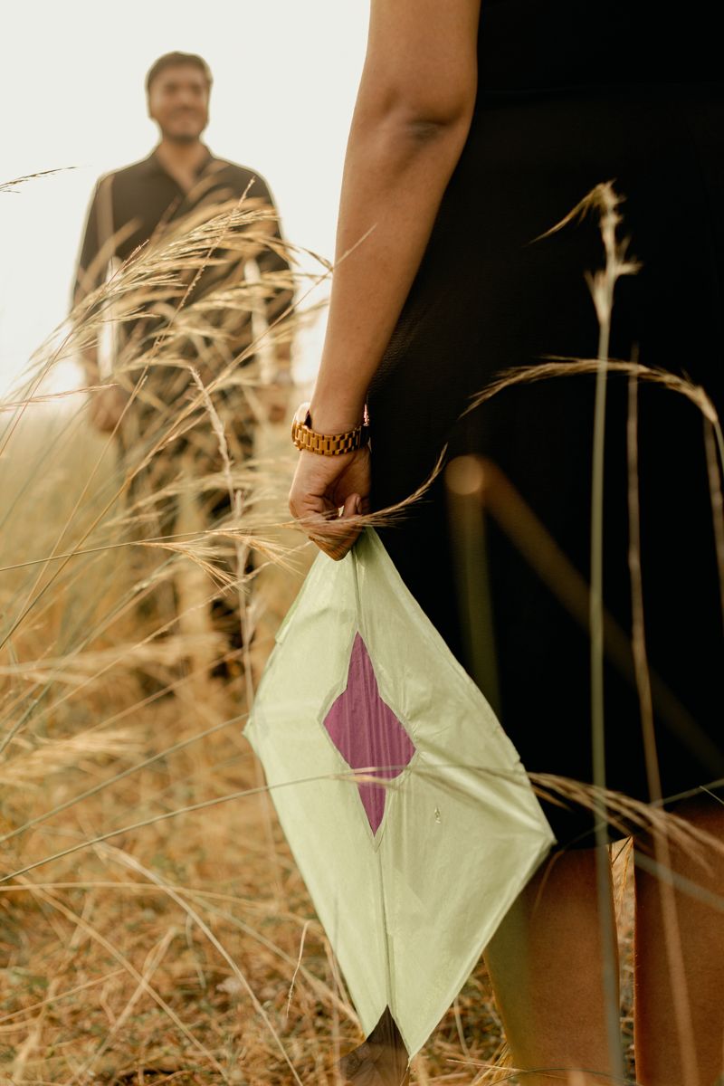 Hand holding a pale green and purple DIY paper kite in a field of tall dry grass during golden hour.
