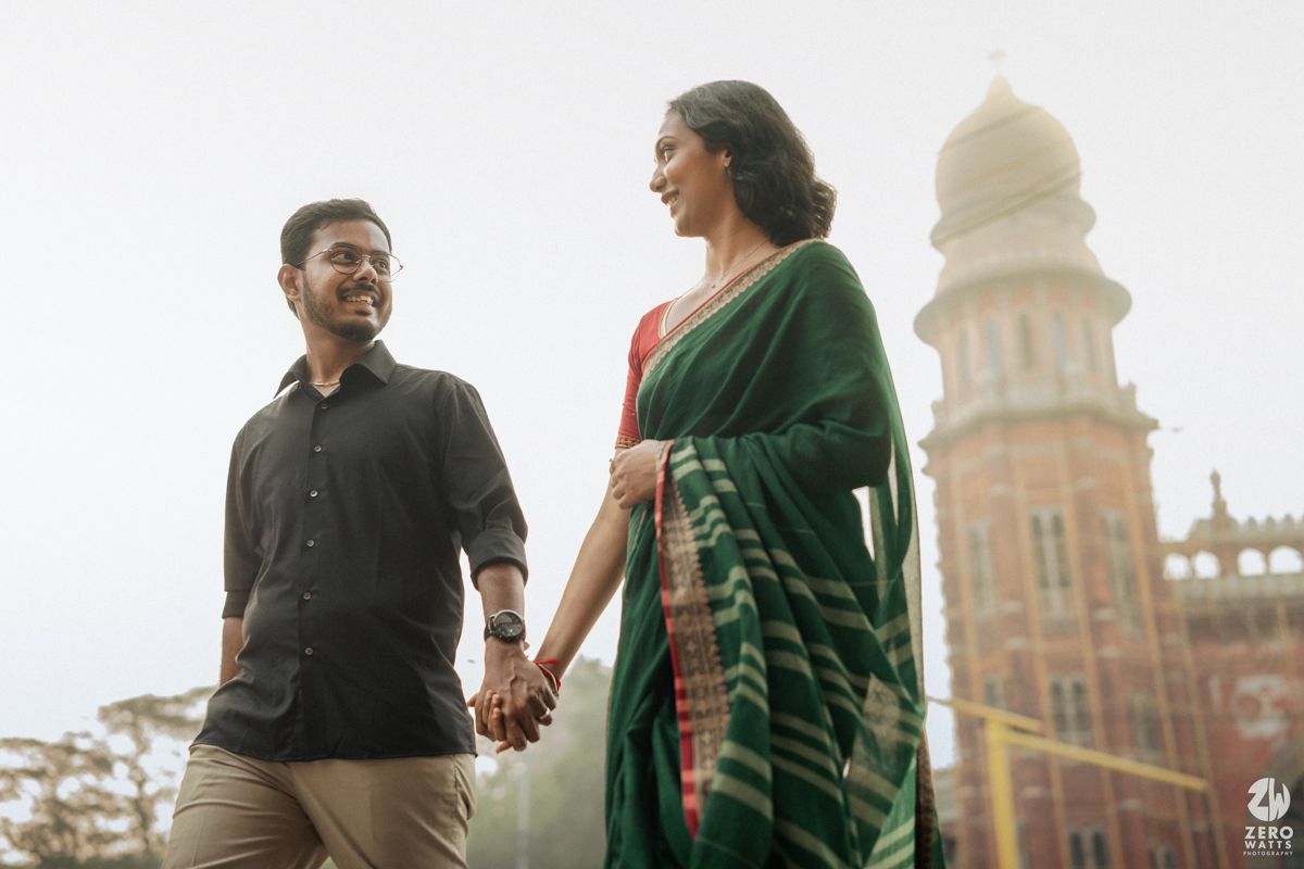 A couple holds hands while standing in front of historic architecture with ornate domes.