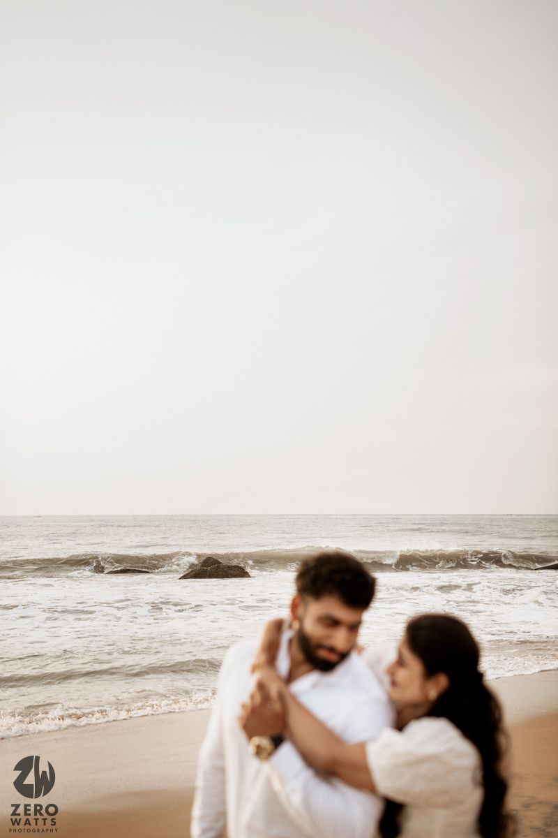 A couple embraces tenderly on a misty beach during an intimate photoshoot.