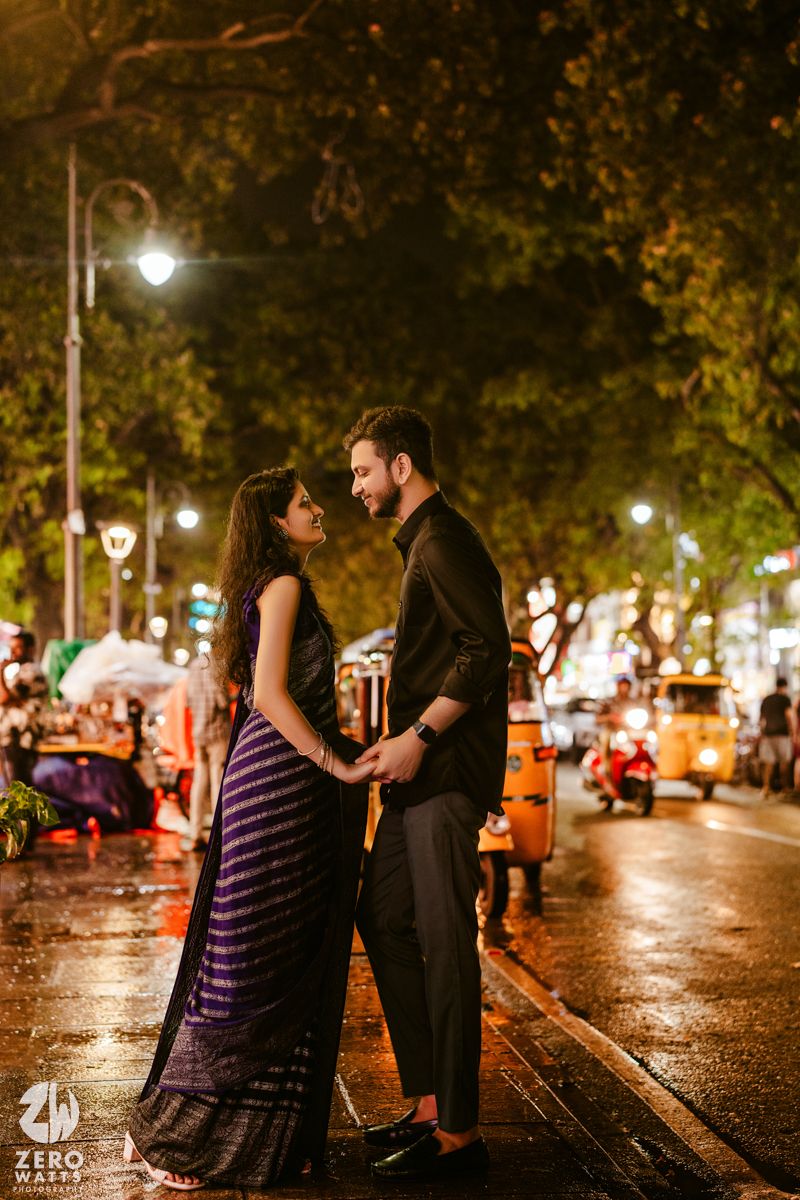 A romantic couple shares an intimate moment on a rainy evening street lit by glowing lamps and autumn trees.