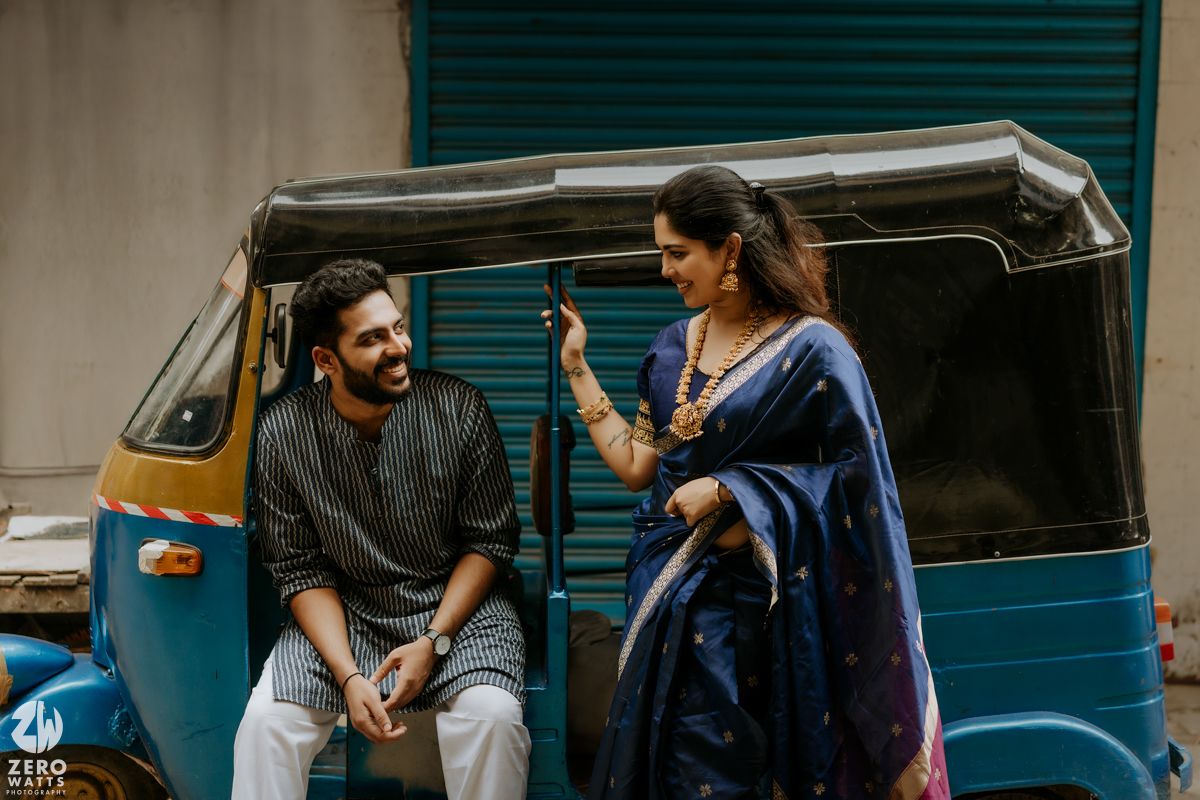 Two people in conversation while sitting on a parked blue auto rickshaw in India.