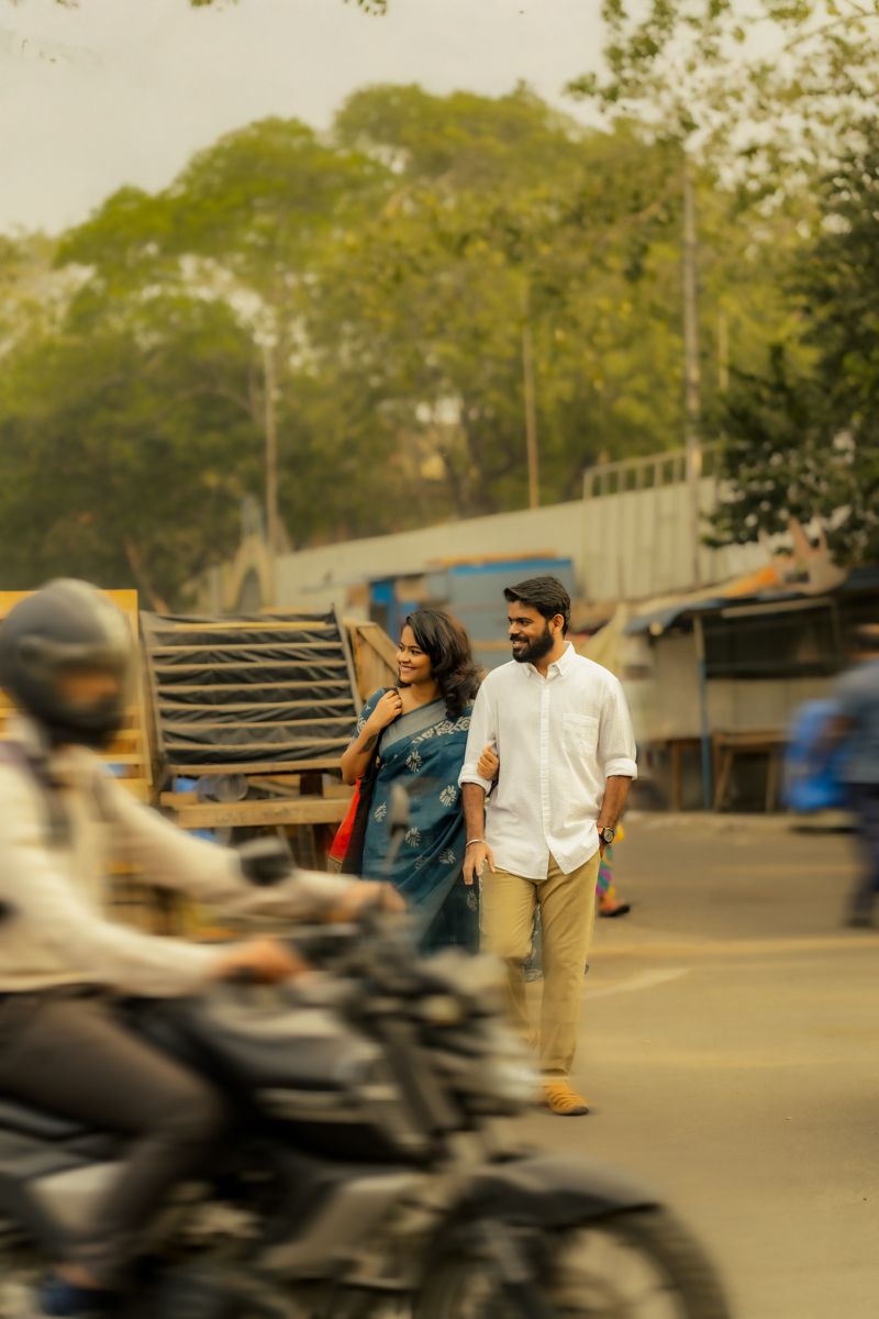 A couple walking together on a busy street with motorcycles passing by in India.
