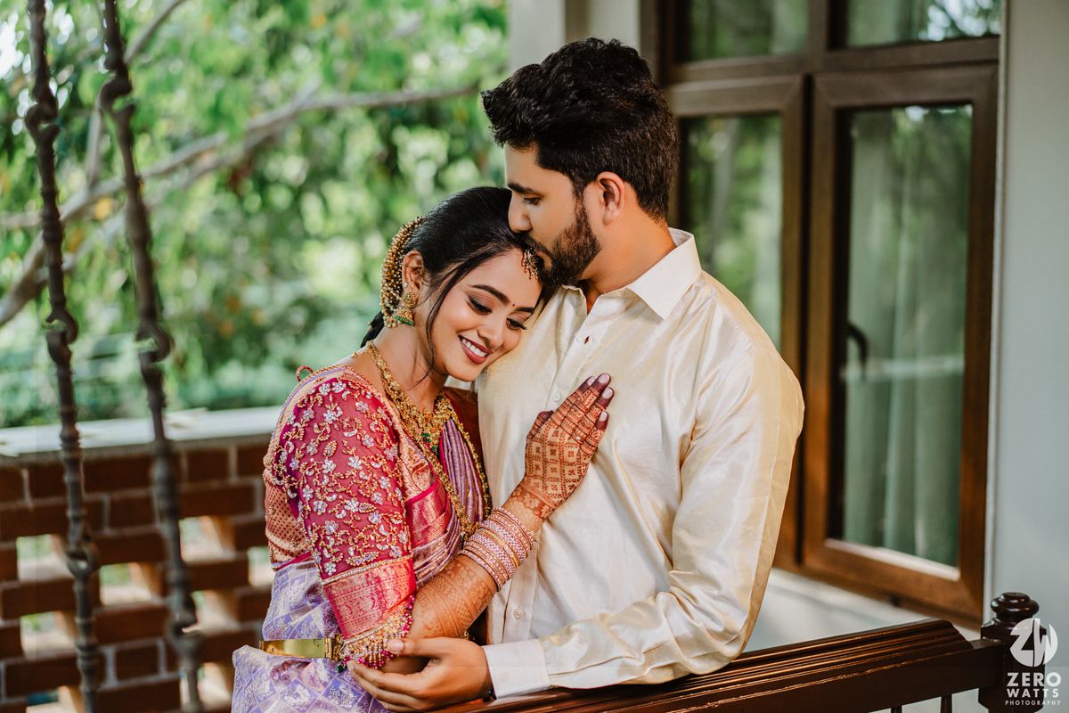A romantic moment between a couple in traditional Indian attire with the bride wearing mehndi and a red floral dress.