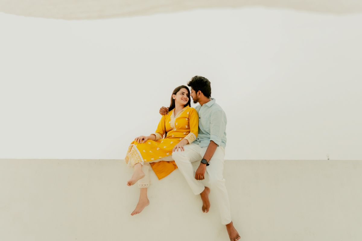 Two people in coordinated yellow and blue outfits sitting together in a minimalist white setting.