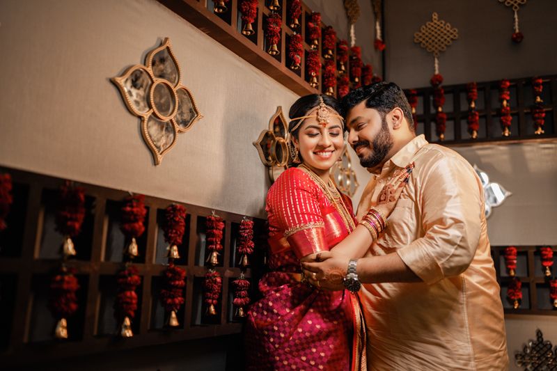 A couple in traditional red and cream attire share an intimate moment during their Indian wedding celebration.