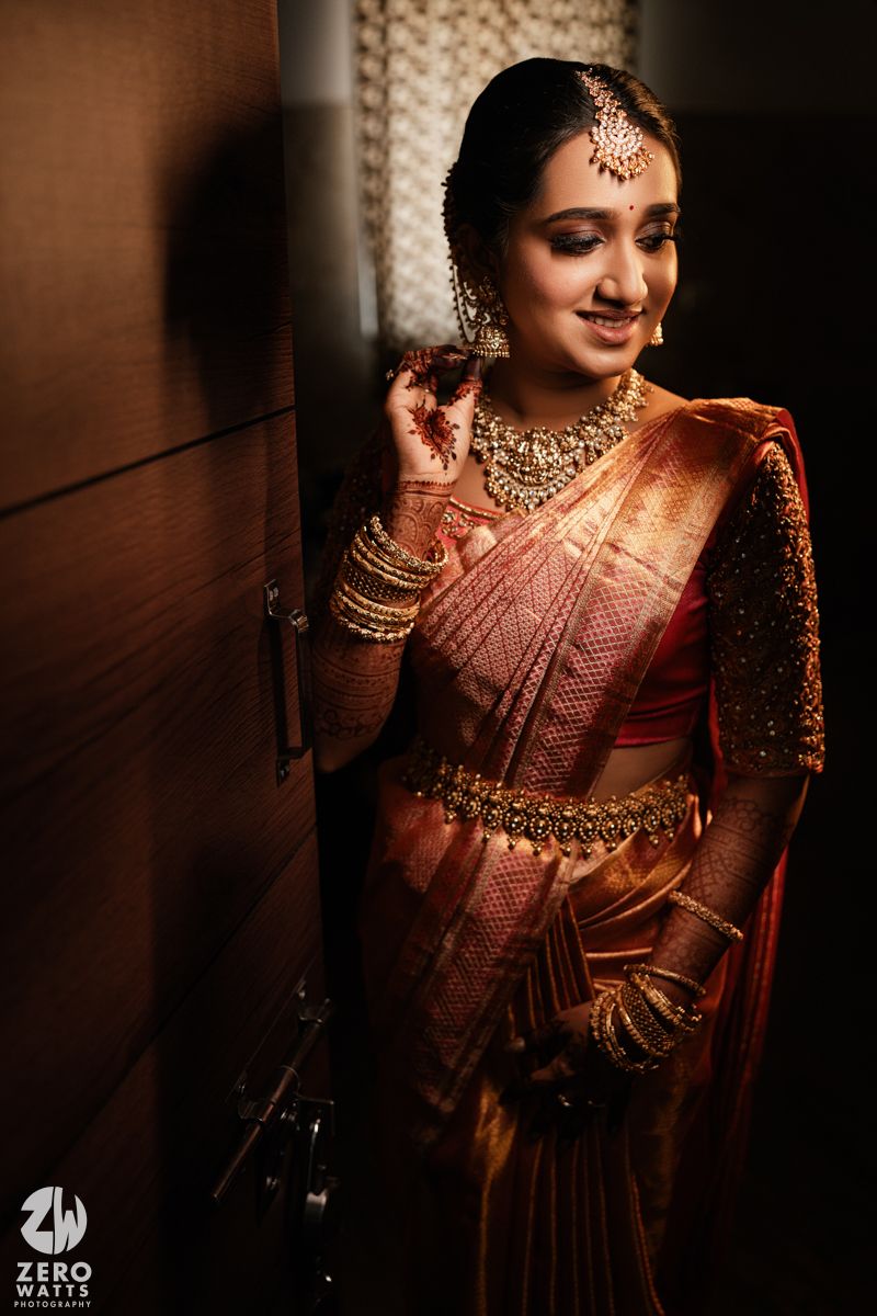 Traditional Indian bridal attire with intricate gold jewelry and red silk saree in moody lighting against dark wood paneling.