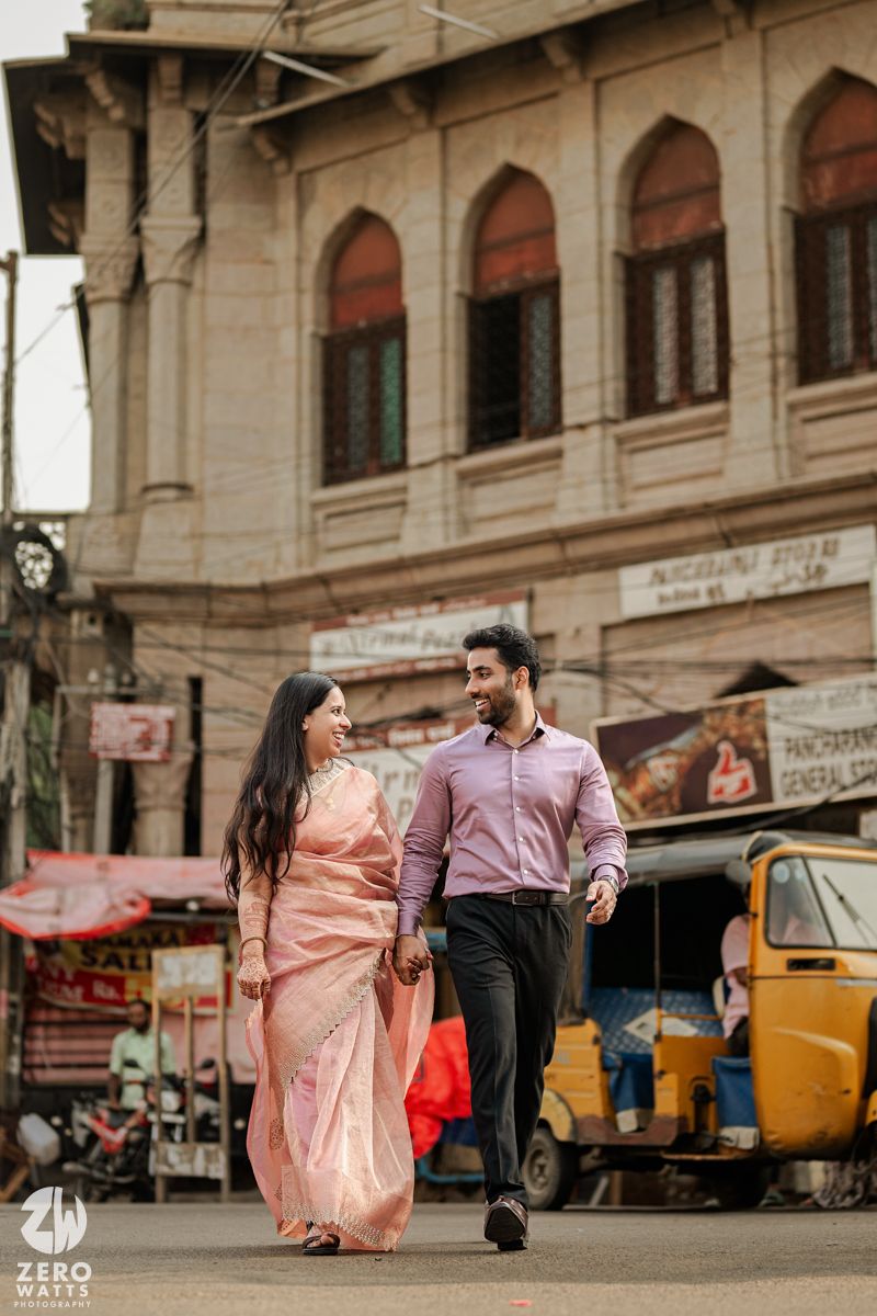 A couple in formal attire strolling through urban streets with vintage buildings and auto rickshaw.