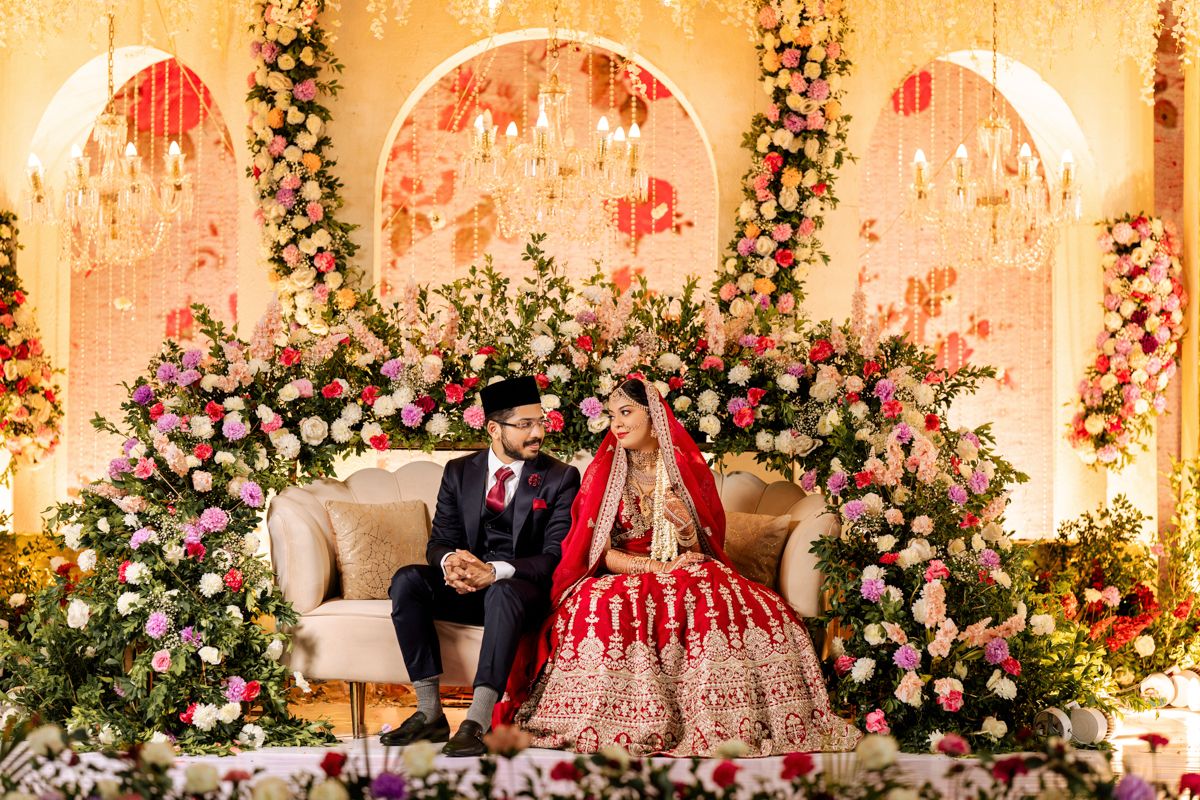 Traditional wedding decor features ornate floral arrangements with pink roses and white blooms against arched backdrops.