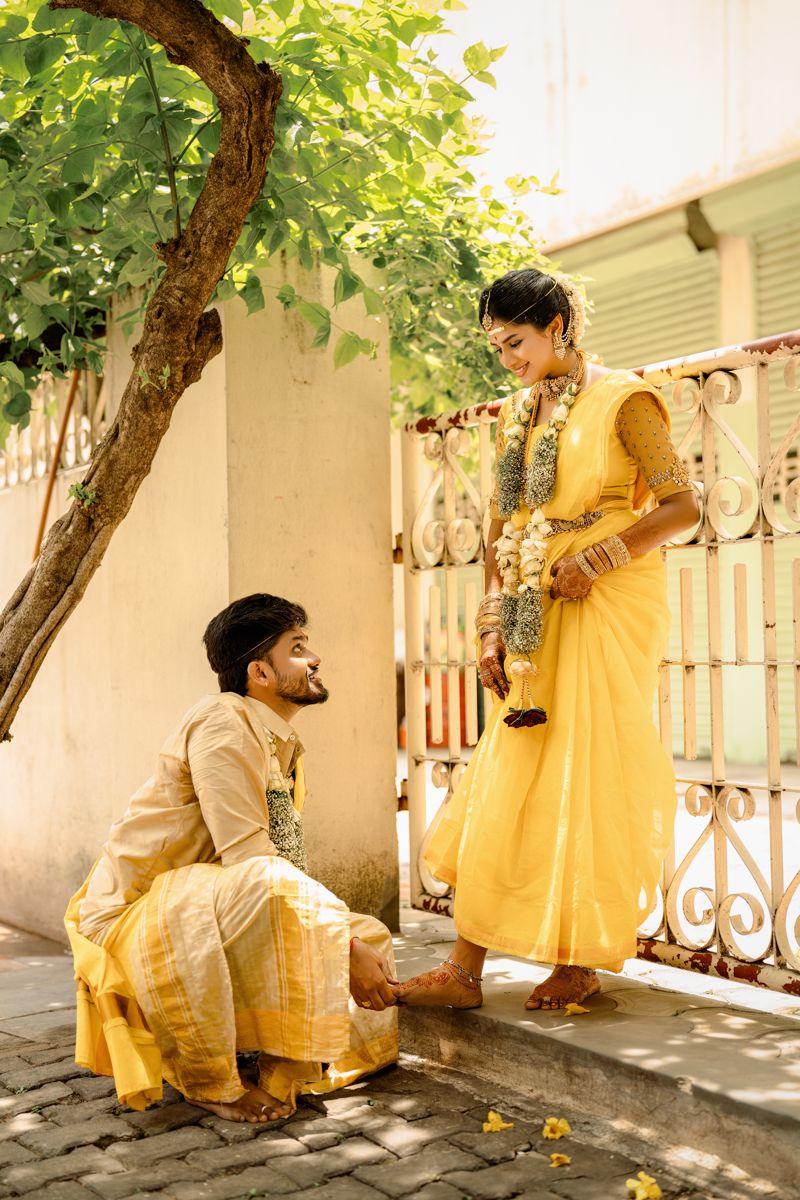 A couple in traditional yellow Indian attire stands on a porch near a tree during a special ceremony.