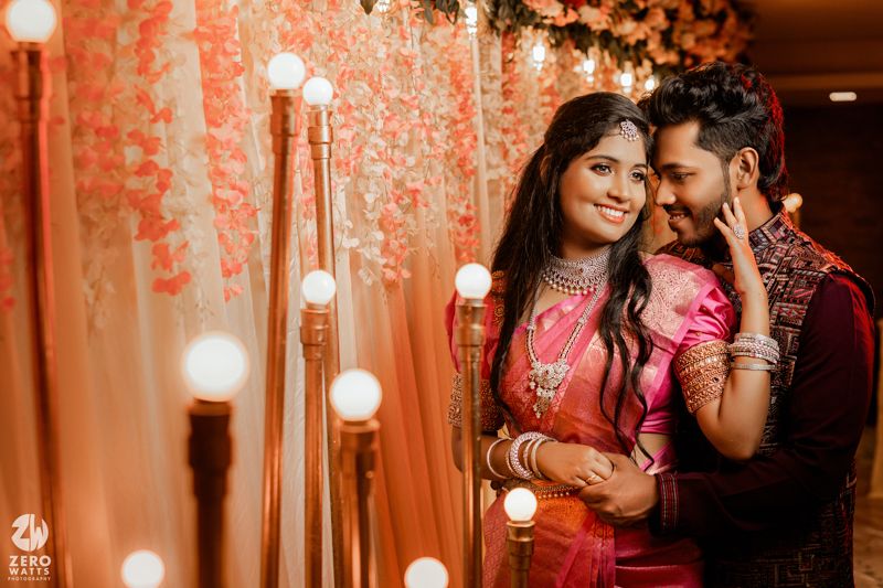 An intimate portrait of a couple in Indian wedding attire sharing a tender moment amidst hanging lights and peach decor.