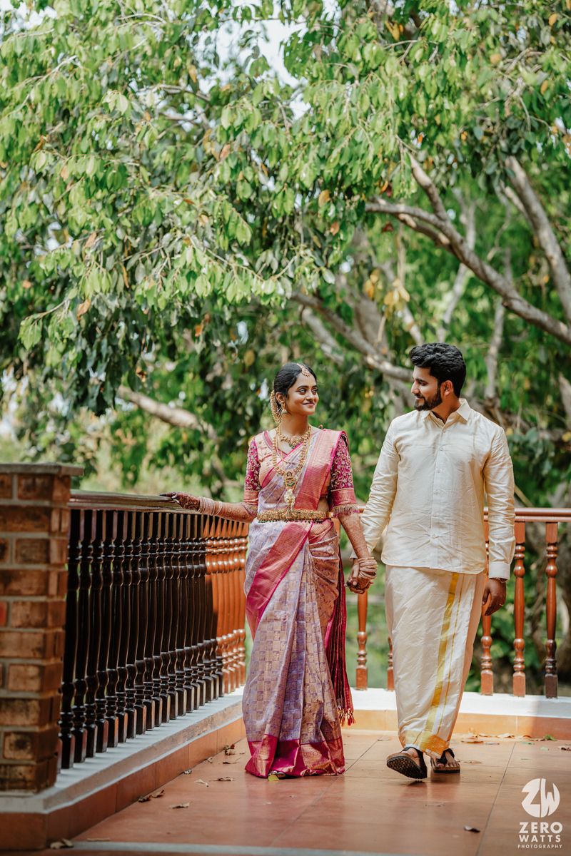 A couple in traditional Indian attire walks along a railed pathway under green eucalyptus trees.
