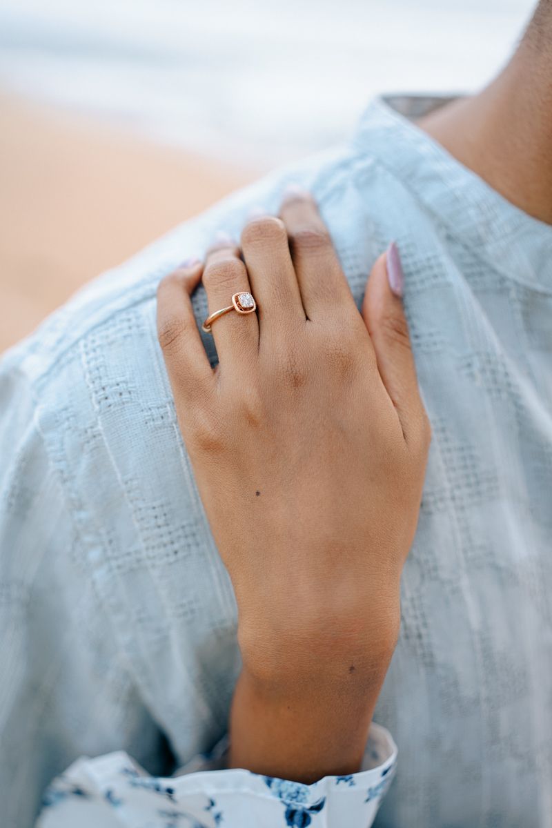 Delicate hand wearing a simple engagement ring against light blue textured fabric.