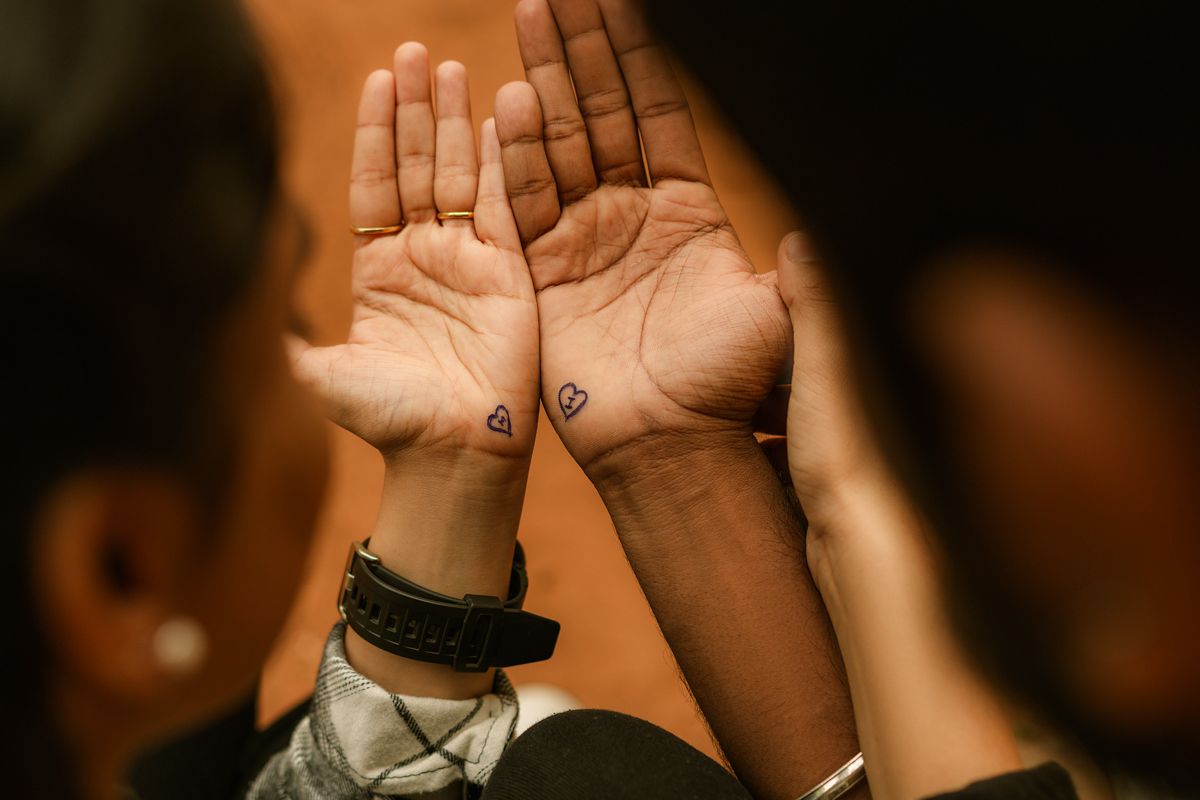 Raised open palms with handwritten text or symbols visible on both hands against a dark background.