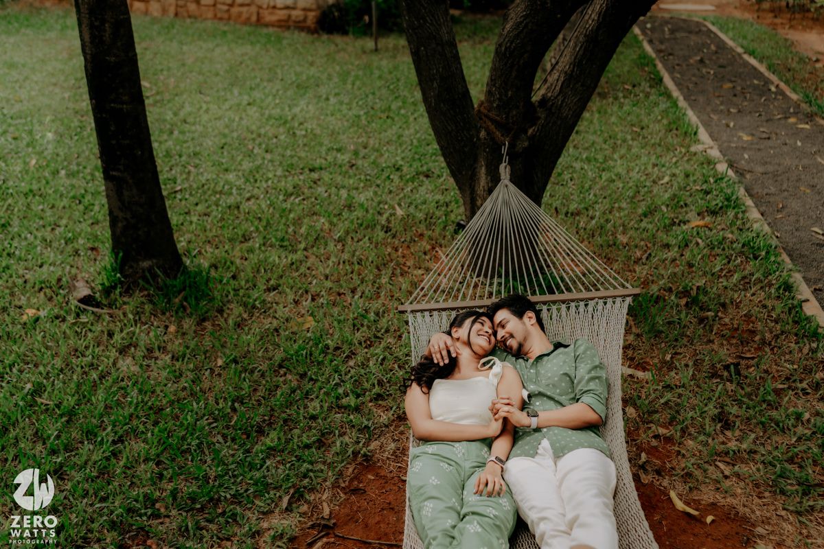 A couple relaxes together in a cozy hammock surrounded by lush green trees in a peaceful outdoor setting.