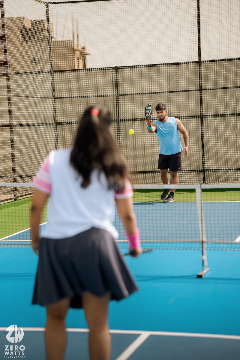 Couple playing sports on an outdoor blue tennis court.