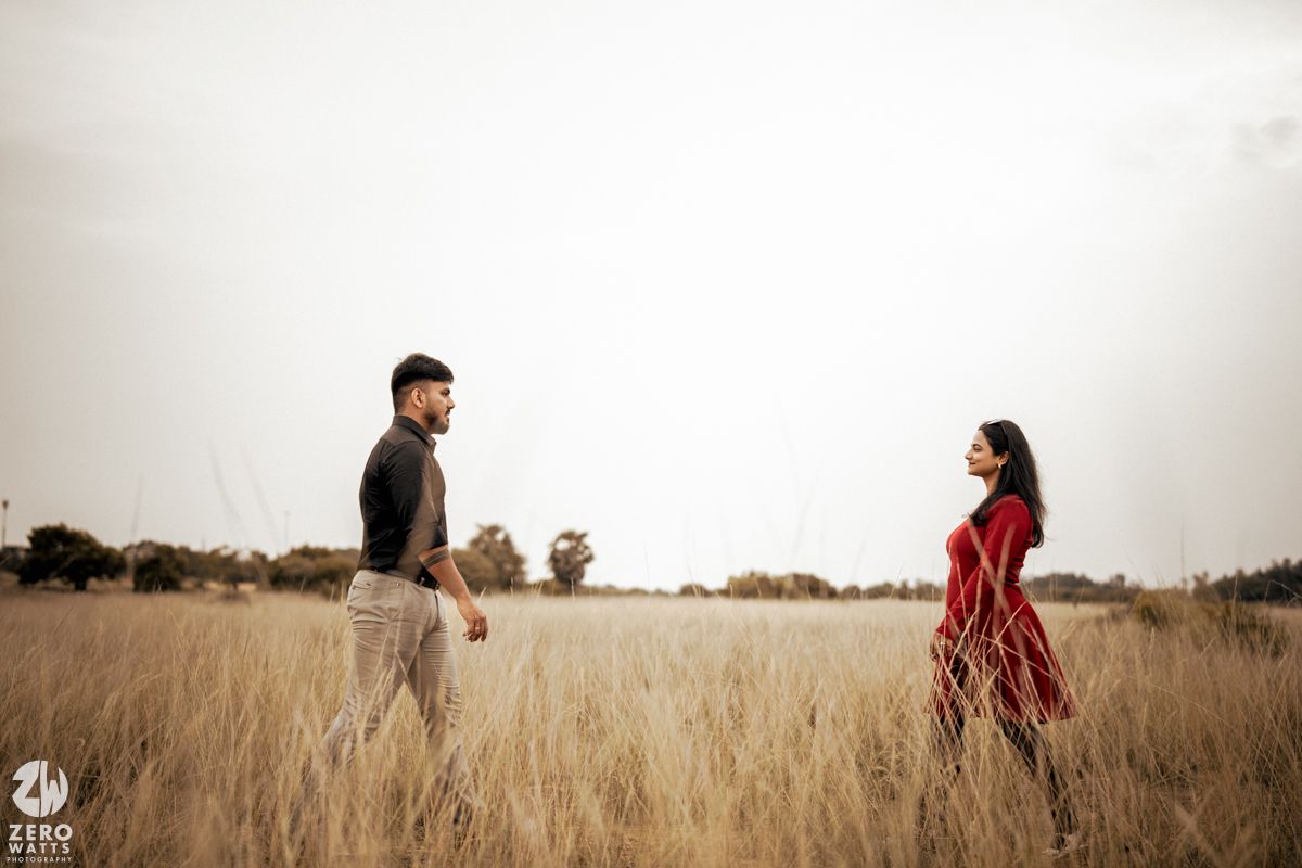 A couple walking apart in opposite directions through a sunlit field of tall grass.