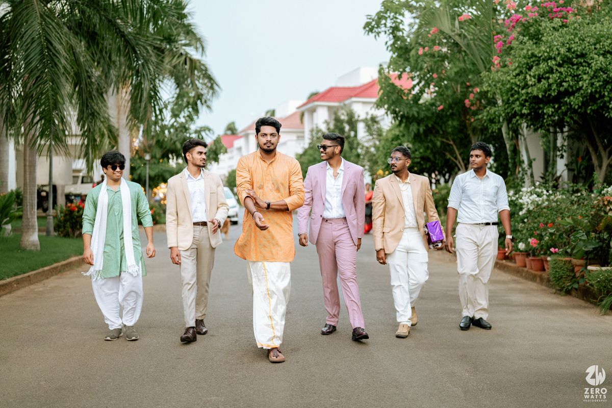 Groomsmen in pastel and white attire walk along a palm-lined pathway during a destination wedding shoot.