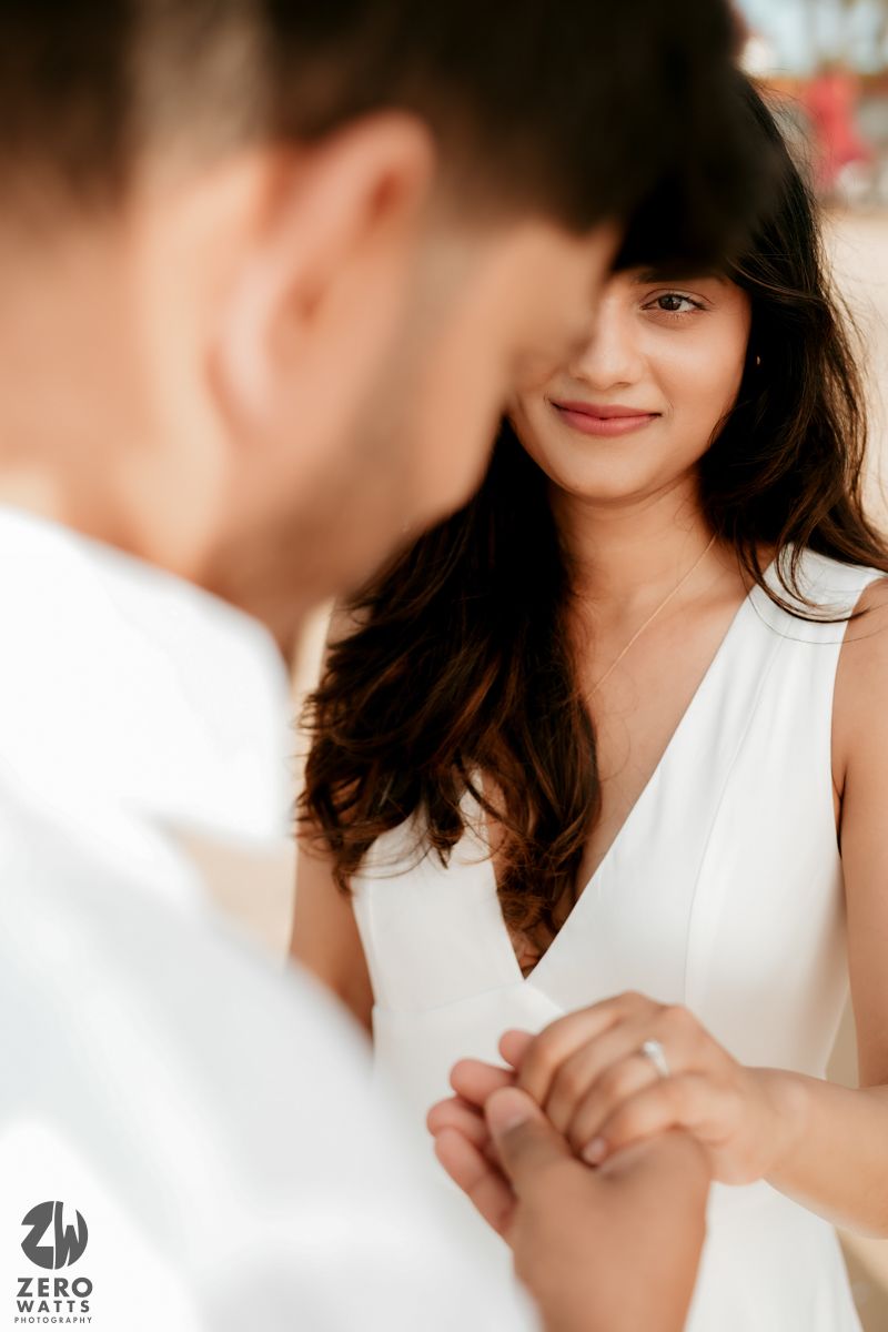 A close up romantic portrait of a couple holding hands and gazing at each other in white attire.