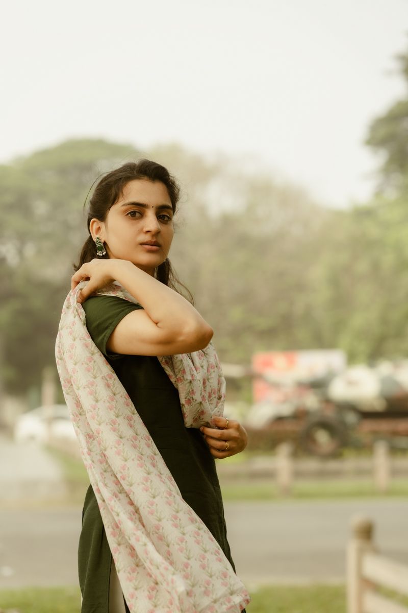 Portrait of person in dark dress and light floral dupatta against blurred outdoor background.