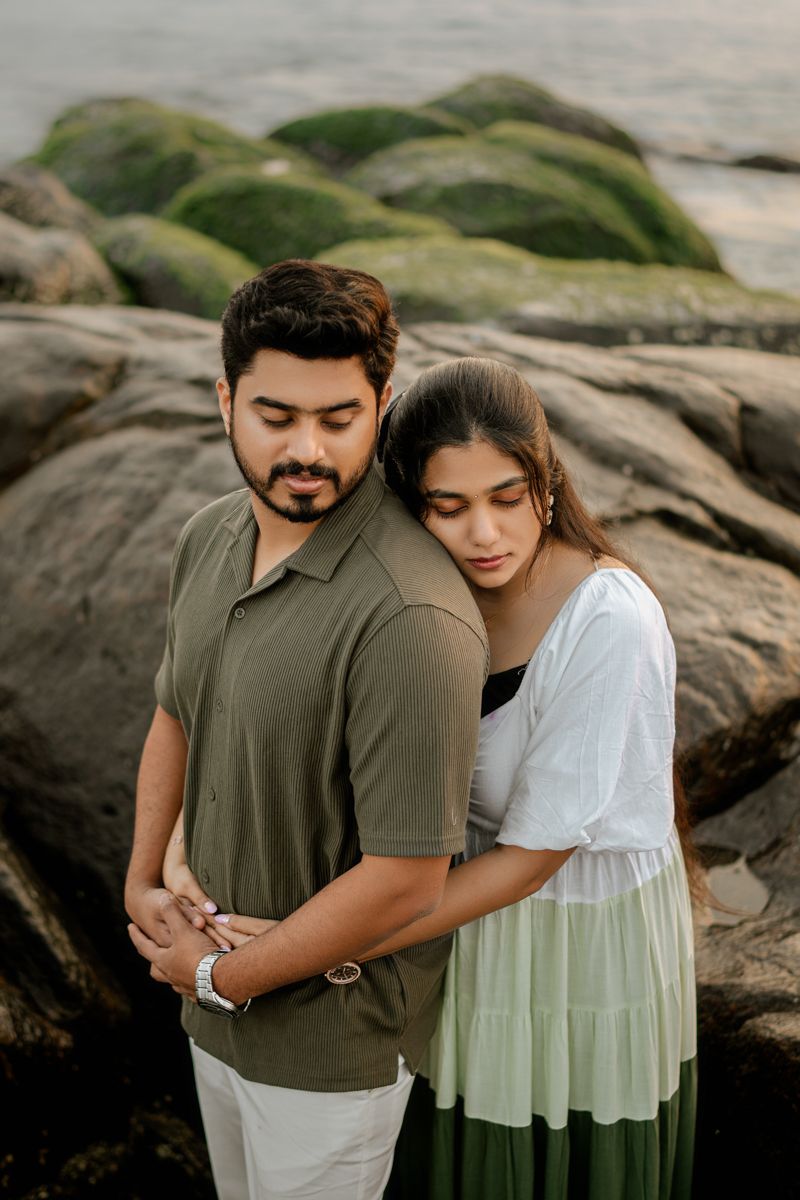 Romantic couple embracing on rocky coastal outcrop during golden hour.