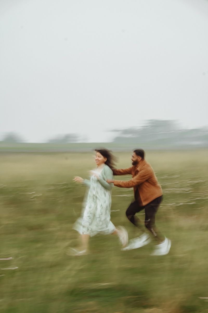 A couple runs together through a misty field in motion blur creating a dreamy romantic atmosphere.