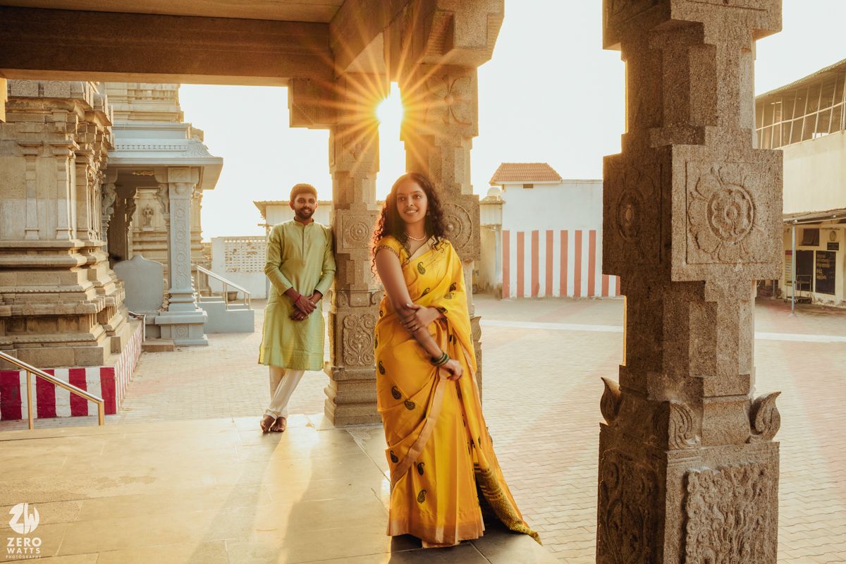 A couple poses in a traditional Indian temple corridor during golden hour with ornate stone pillars.