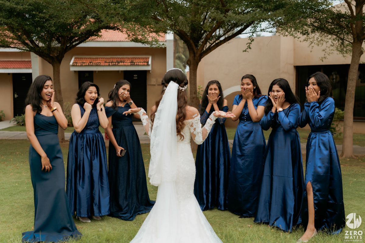 Wedding party wearing elegant navy blue bridesmaid dresses reacts with joy on a grassy lawn outside.