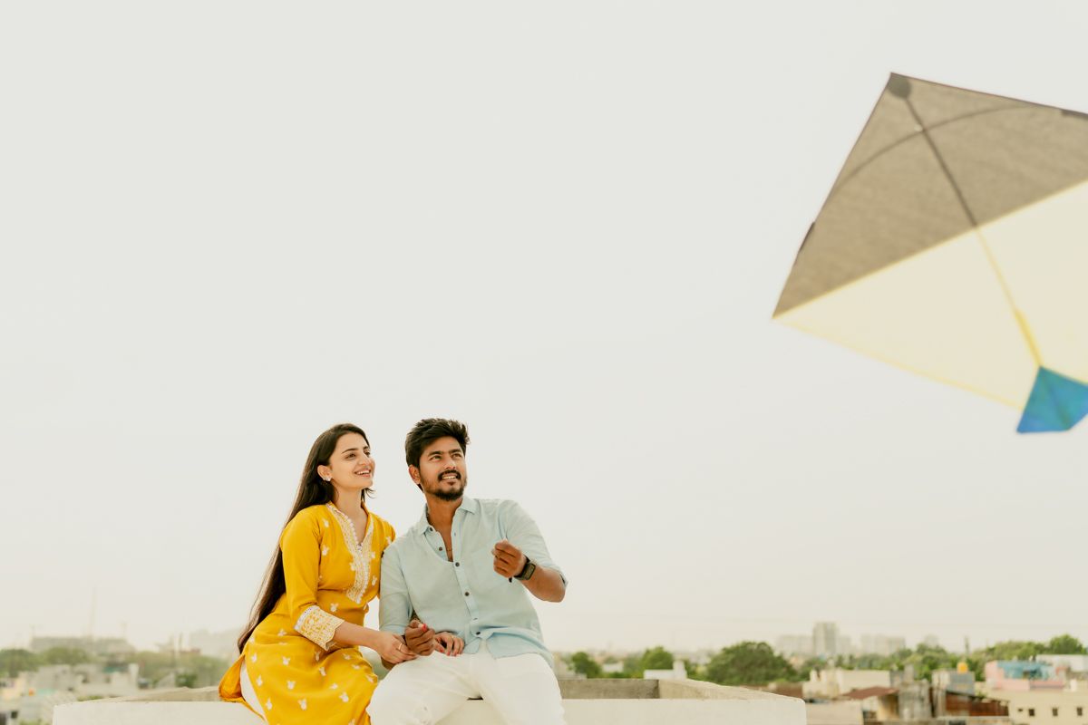 A couple in yellow and pastel outfits playing with a kite on a rooftop at sunset.