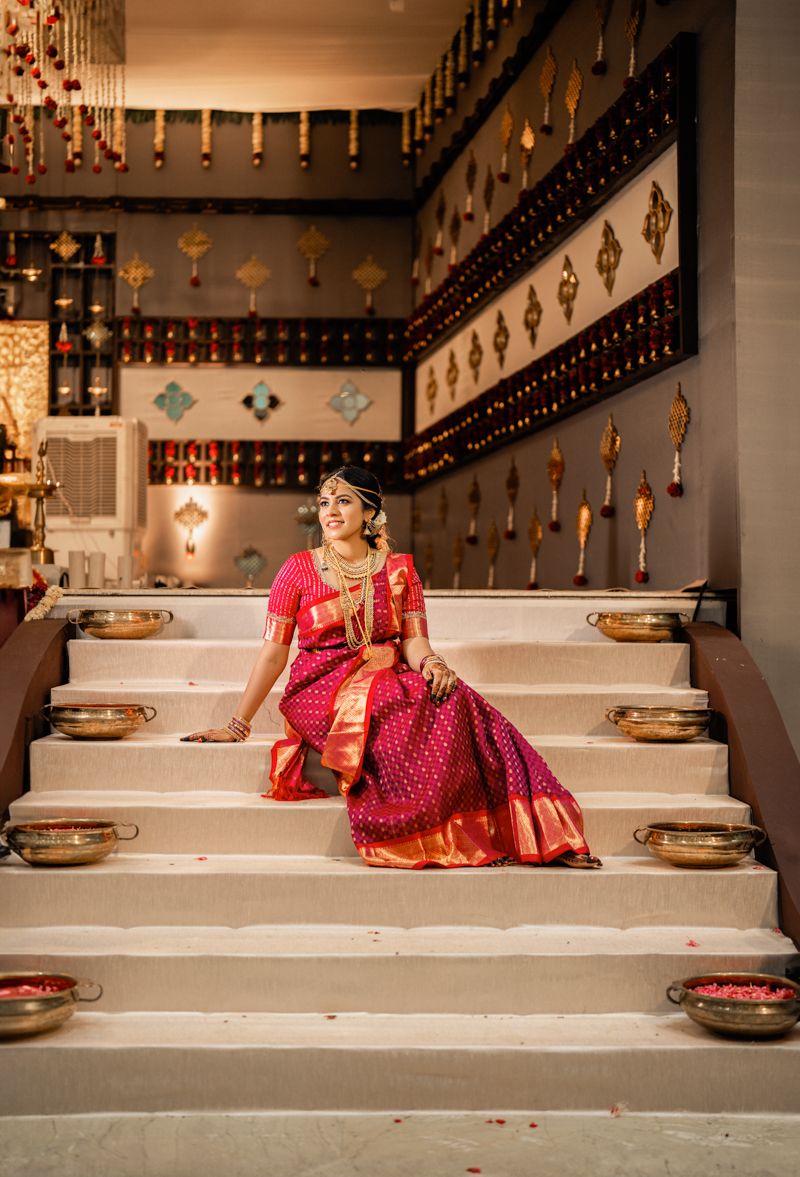 Ornate wedding setting with red silk sari on white marble steps adorned with traditional brass diyas and decorative walls.