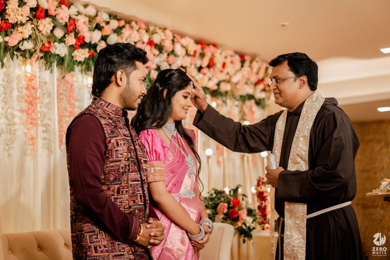 A traditional Indian ceremony blessing taking place under a floral backdrop with pink and white flowers.
