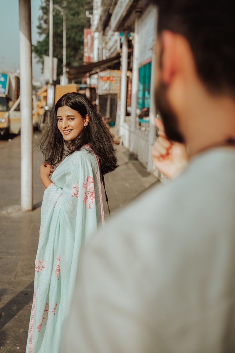 A person in a mint green floral saree smiles while being photographed on a city street.
