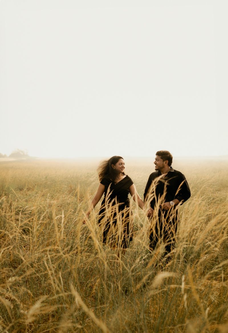 Two people stand together in tall grass during golden hour, sharing a joyful moment in nature.