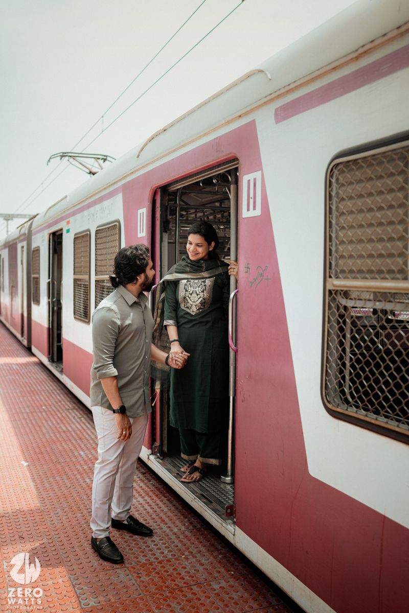 A couple interacts through an open train door painted in maroon and white colors.