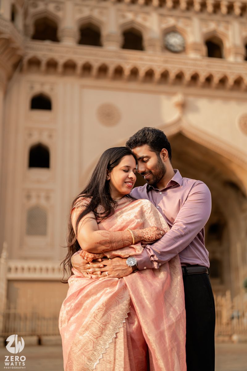A romantic couple shares an intimate moment in front of ornate architecture during a photoshoot.