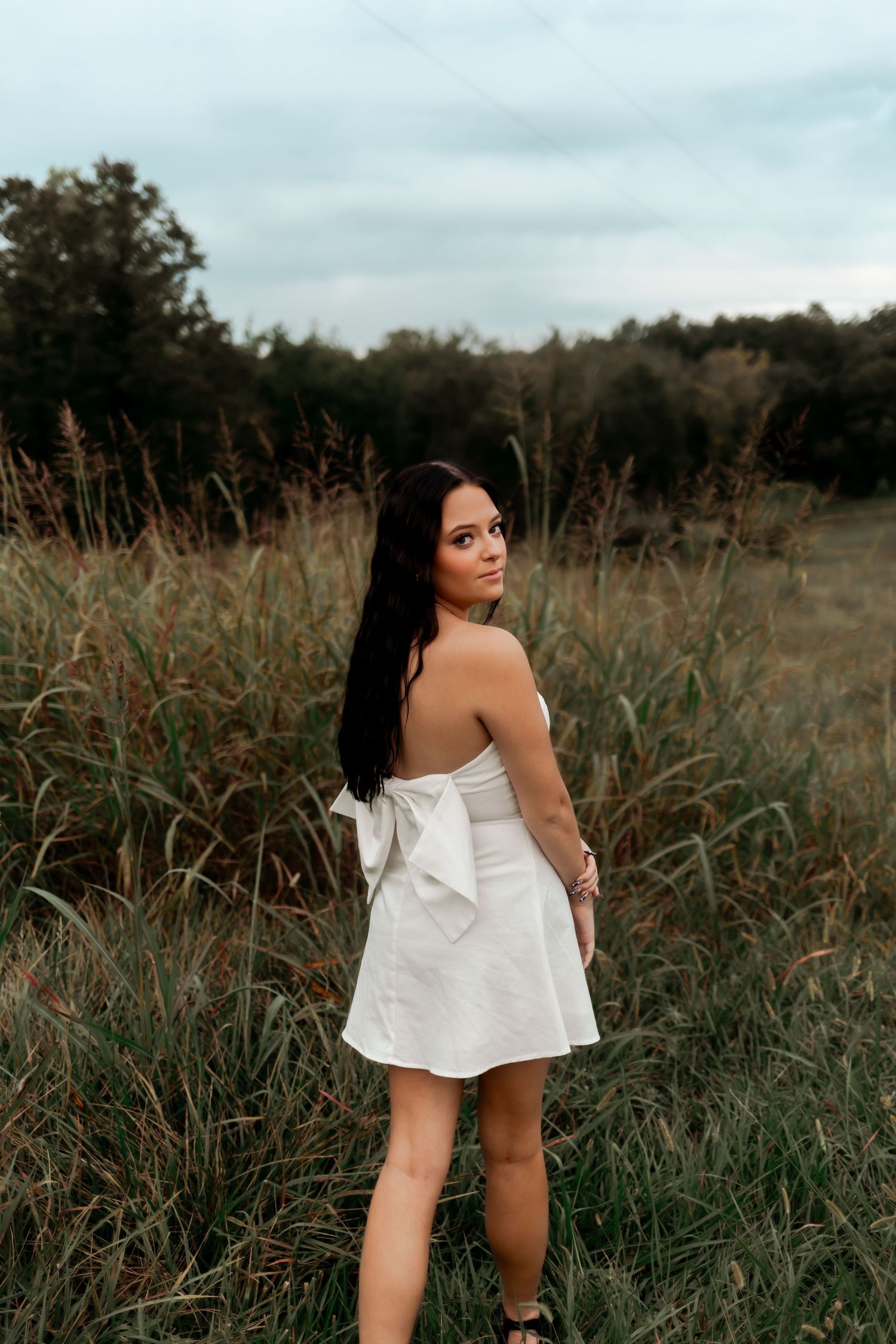 A woman in a white dress stands in a field of tall grass during golden hour.