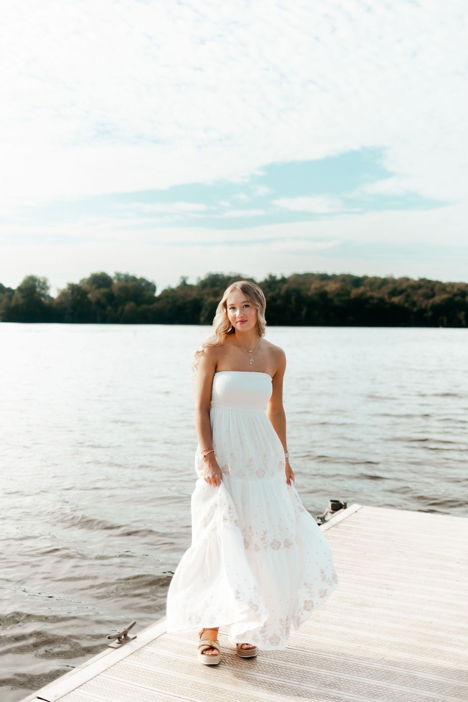 White maxi dress photoshoot on wooden dock by serene lake.
