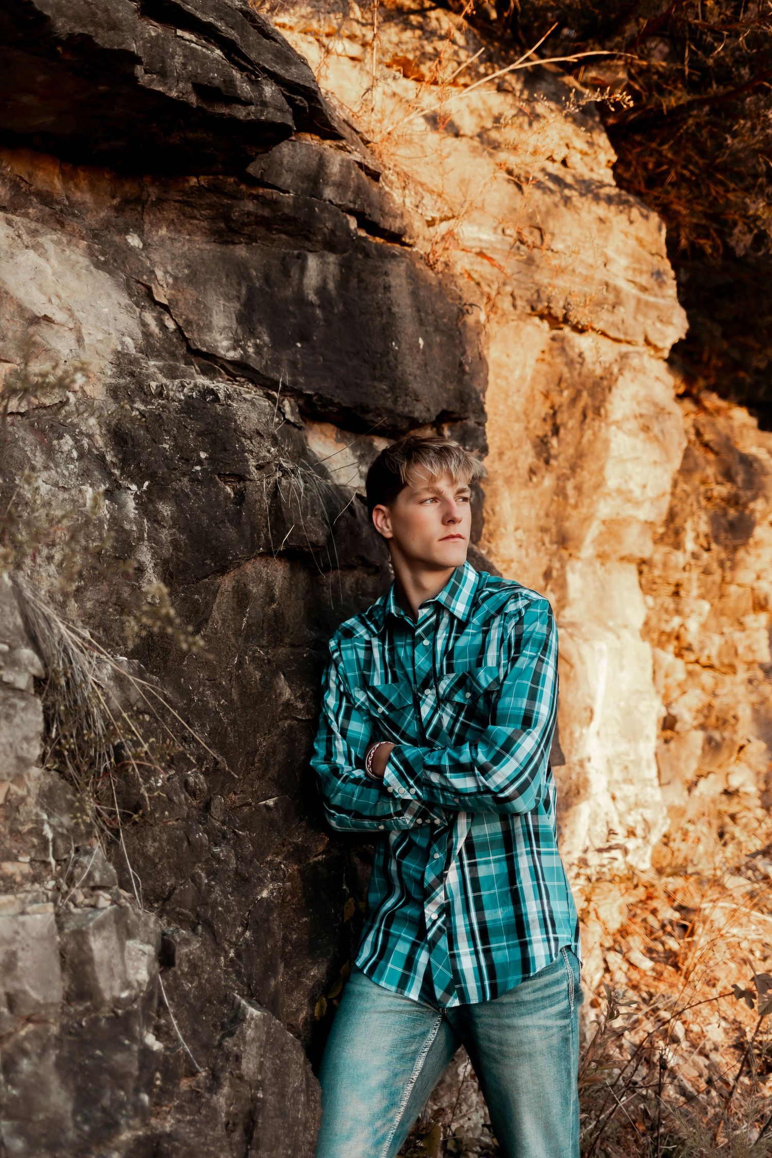A person in a plaid turquoise shirt leans against a textured rock wall.
