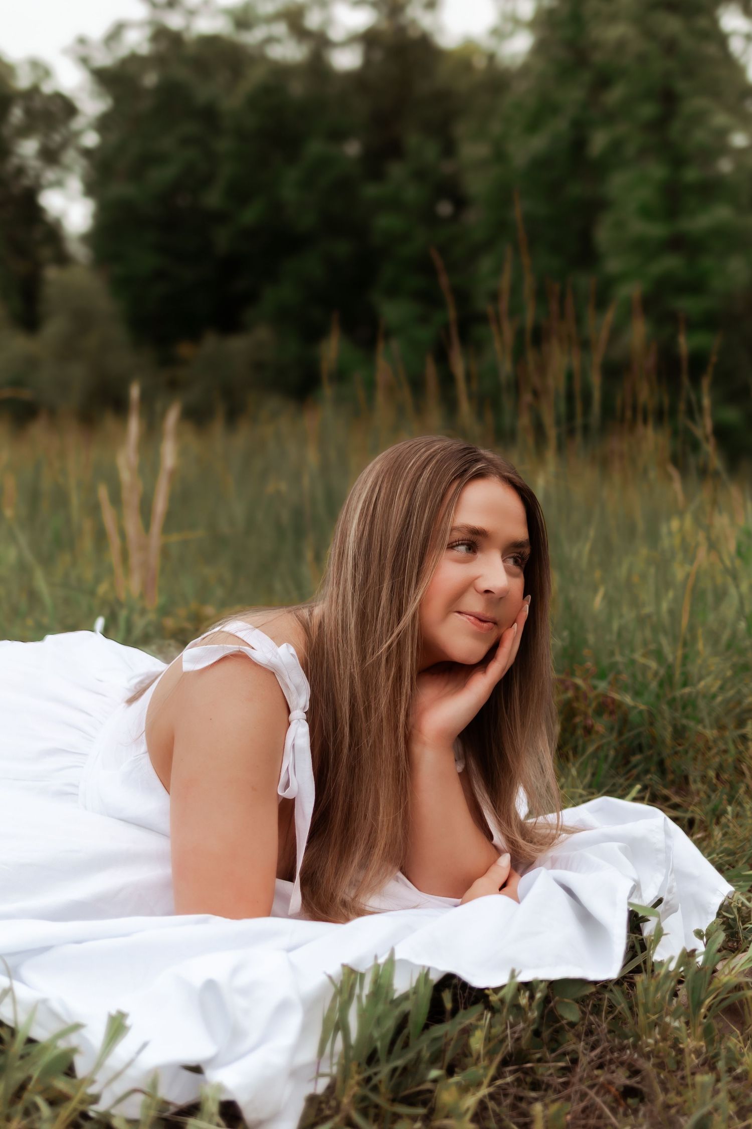 Dreamy portrait of person lying on white blanket in tall grass.