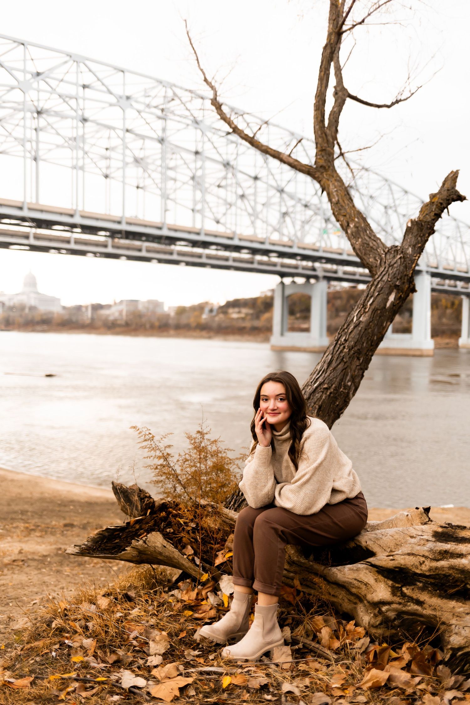 An autumn portrait by a river with a bridge and fallen leaves in the background.