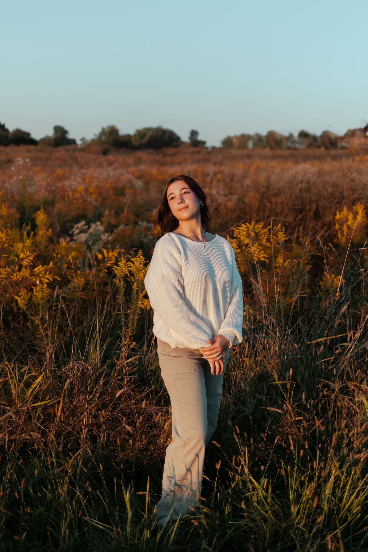 Someone wearing a cozy white sweater stands in a field of dried autumn grasses against a blue sky.